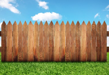 Wooden fence and green grass under blue sky with clouds outdoors