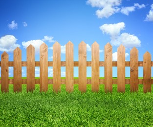 Wooden fence and green grass under blue sky with clouds outdoors