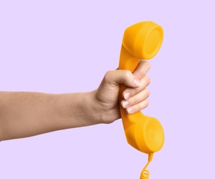 Woman holding yellow telephone handset on light violet background, closeup