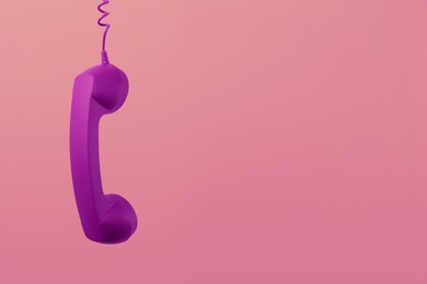Image of Purple telephone handset hanging on pink background. Space for text