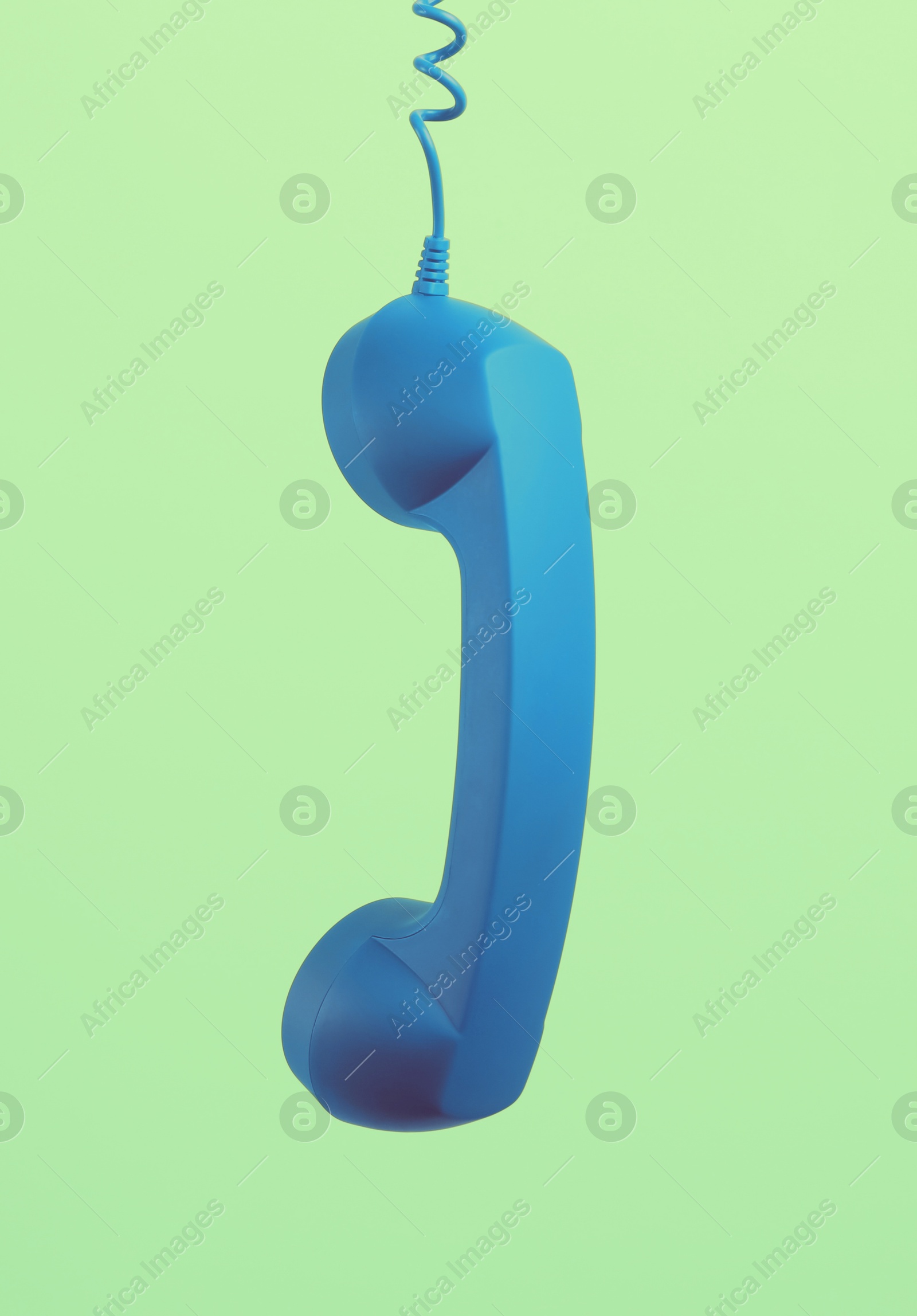 Image of Blue telephone handset hanging on light green background. Space for text