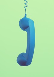 Image of Blue telephone handset hanging on light green background. Space for text