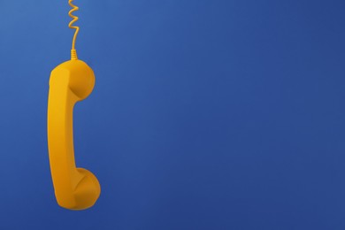 Image of Orange telephone handset hanging on blue background. Space for text