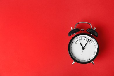 Image of Black alarm clock with hands pointing at numbers 2024 and 2025 on red background, top view. Beginning of new year