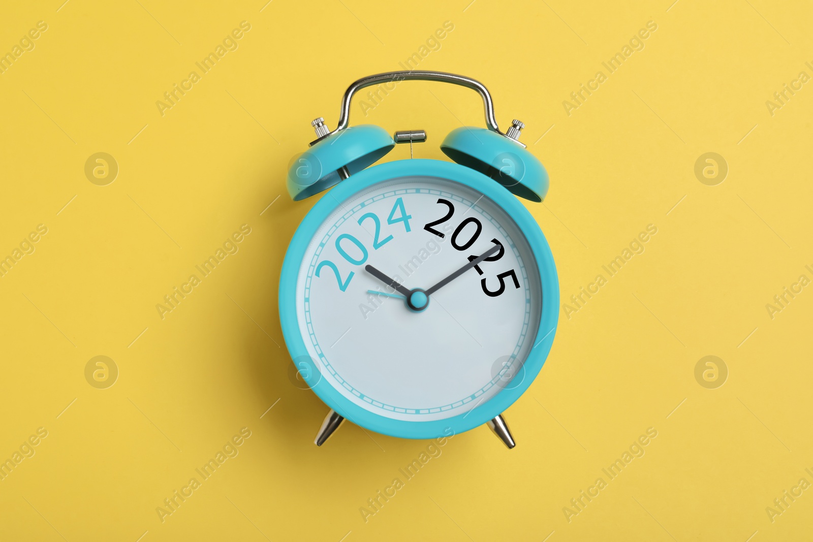 Image of Alarm clock with hands pointing at numbers 2024 and 2025 on yellow background, top view. Beginning of new year