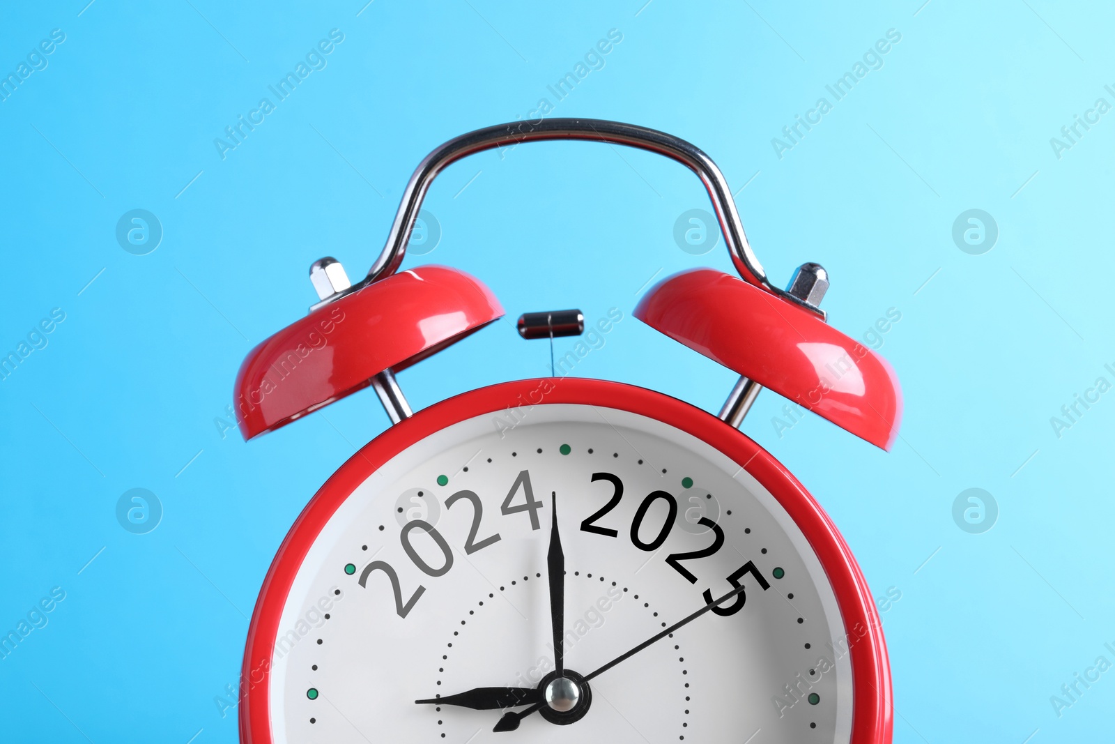 Image of Red alarm clock with numbers 2024 and 2025 on light blue background, closeup. Beginning of new year