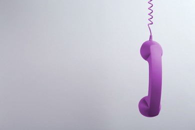 Purple telephone handset hanging on light grey background. Space for text