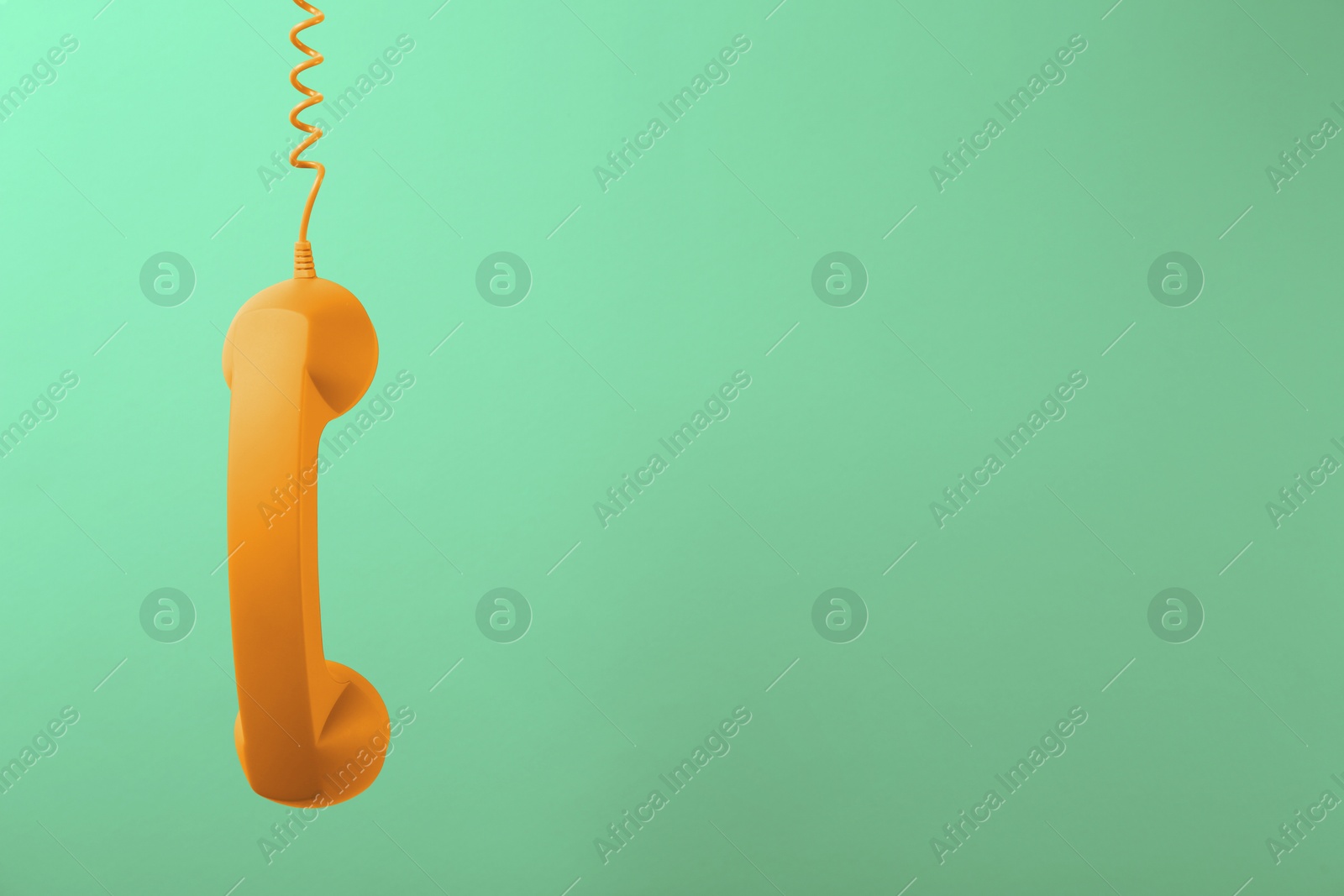 Image of Orange telephone handset hanging on light green background. Space for text