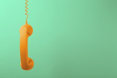 Image of Orange telephone handset hanging on light green background. Space for text