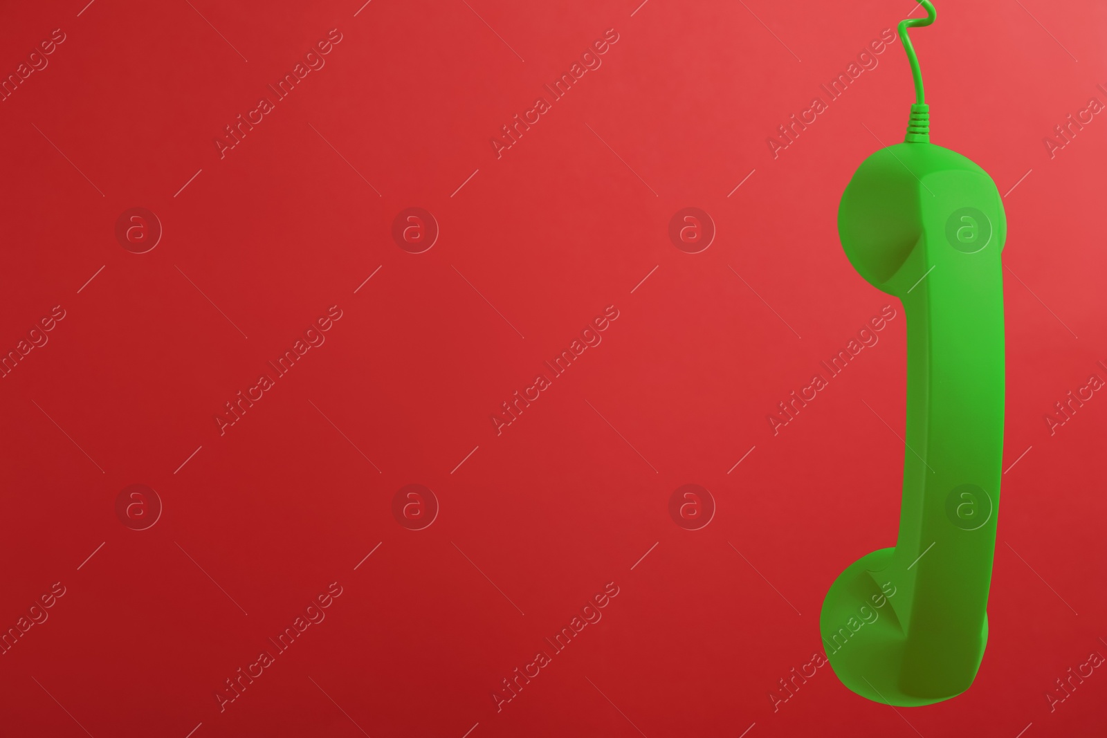 Image of Green telephone handset hanging on red background. Space for text