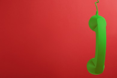Image of Green telephone handset hanging on red background. Space for text