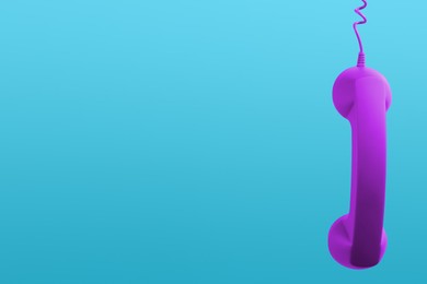 Image of Purple telephone handset hanging on light blue background. Space for text