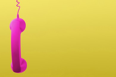 Magenta telephone handset hanging on yellow background. Space for text
