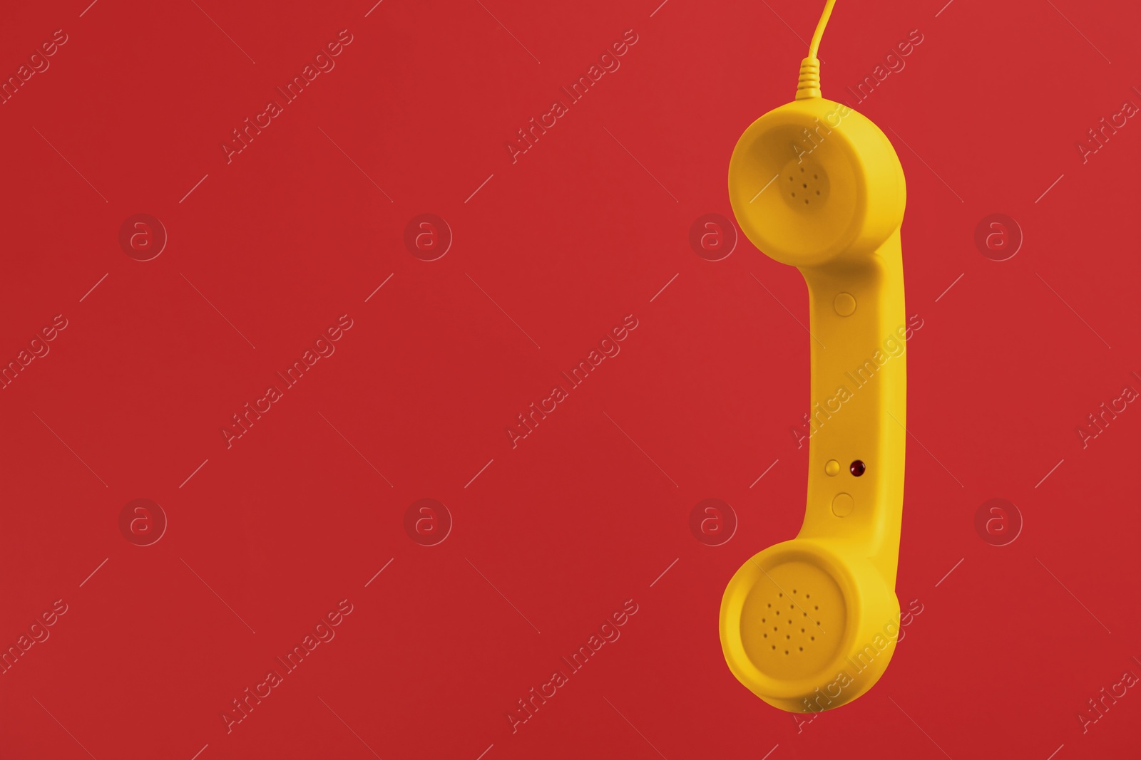 Image of Yellow telephone handset hanging on red background. Space for text
