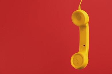 Yellow telephone handset hanging on red background. Space for text