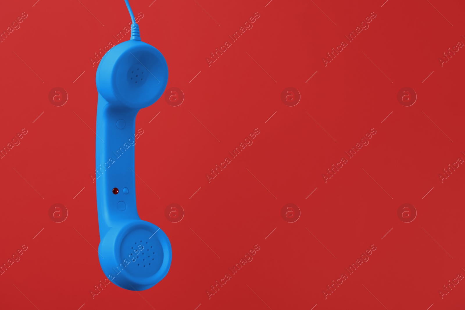 Image of Blue telephone handset hanging on red background. Space for text