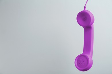 Image of Purple telephone handset hanging on light grey background. Space for text