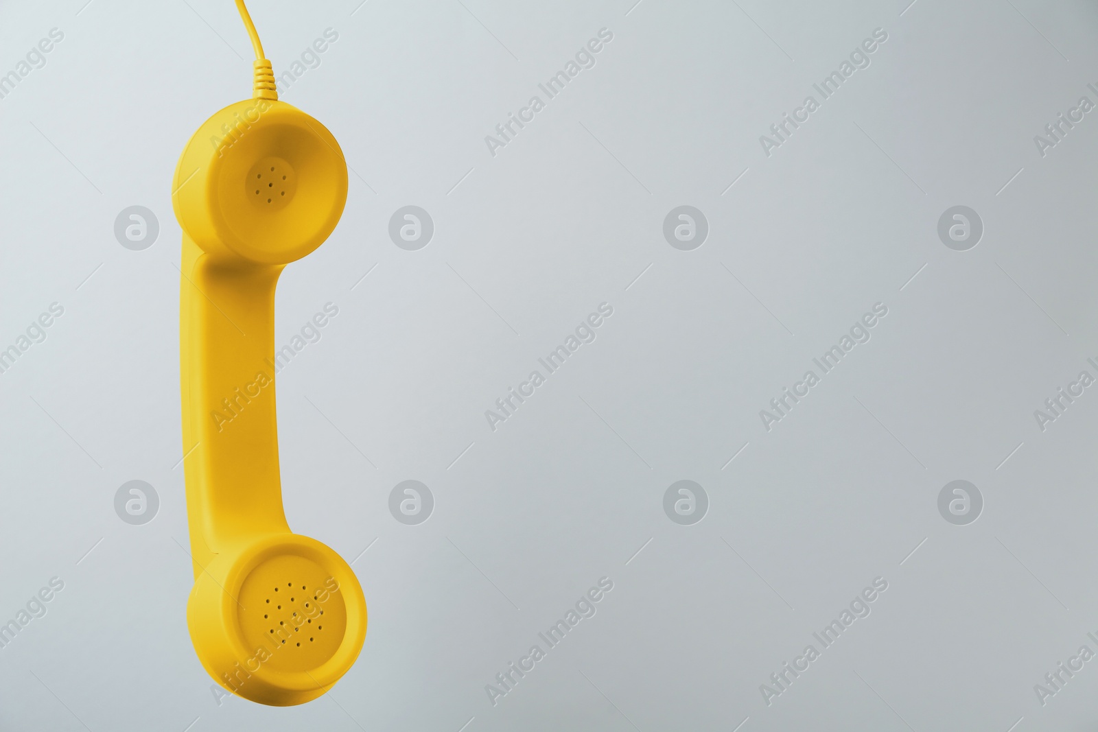 Image of Yellow telephone handset hanging on light grey background. Space for text