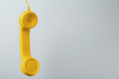 Yellow telephone handset hanging on light grey background. Space for text
