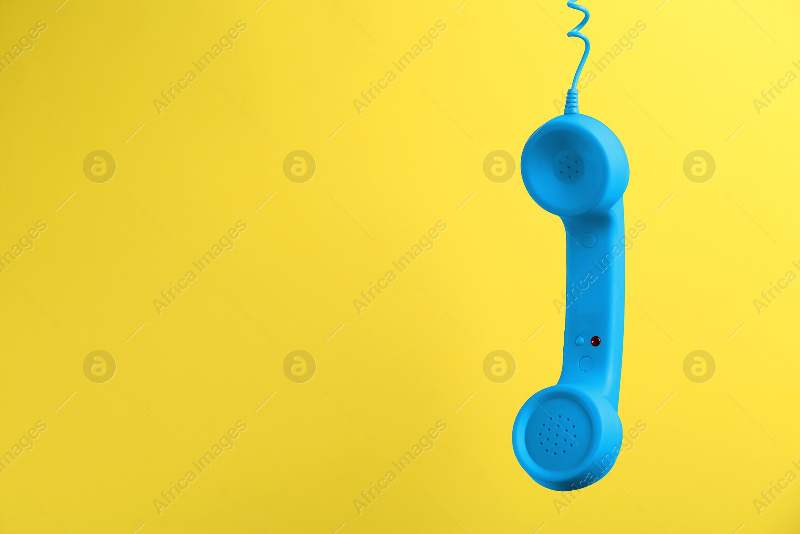 Image of Blue telephone handset hanging on yellow background. Space for text