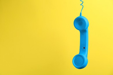 Image of Blue telephone handset hanging on yellow background. Space for text