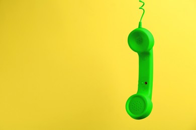 Green telephone handset hanging on yellow background. Space for text