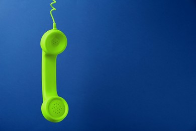 Green telephone handset hanging on blue background. Space for text