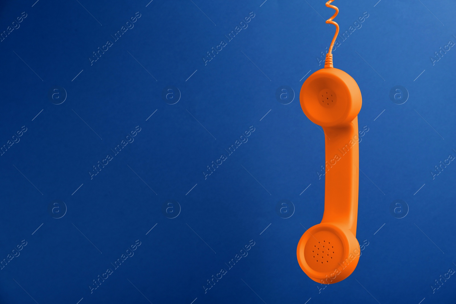 Image of Orange telephone handset hanging on blue background. Space for text