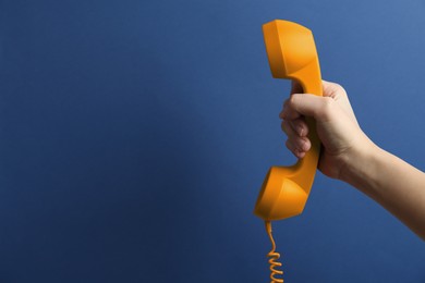 Image of Woman holding orange telephone handset on blue background, closeup. Space for text