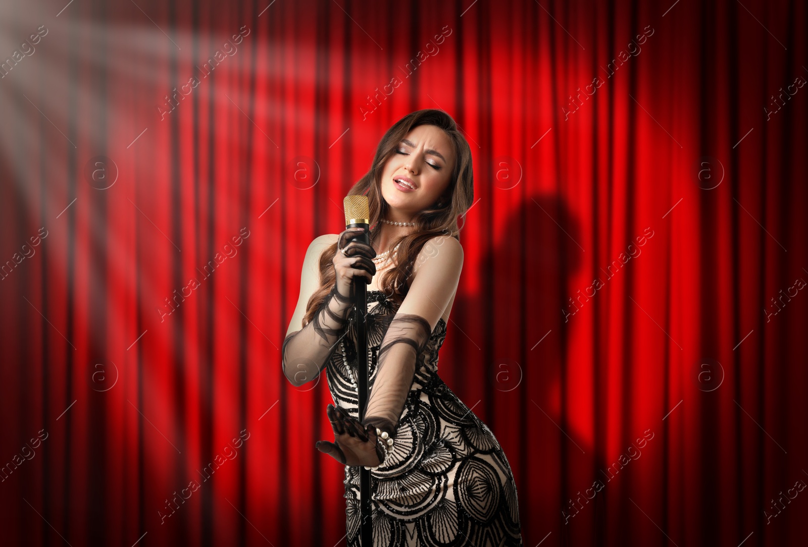 Image of Beautiful singer performing in spotlight on stage against red curtain