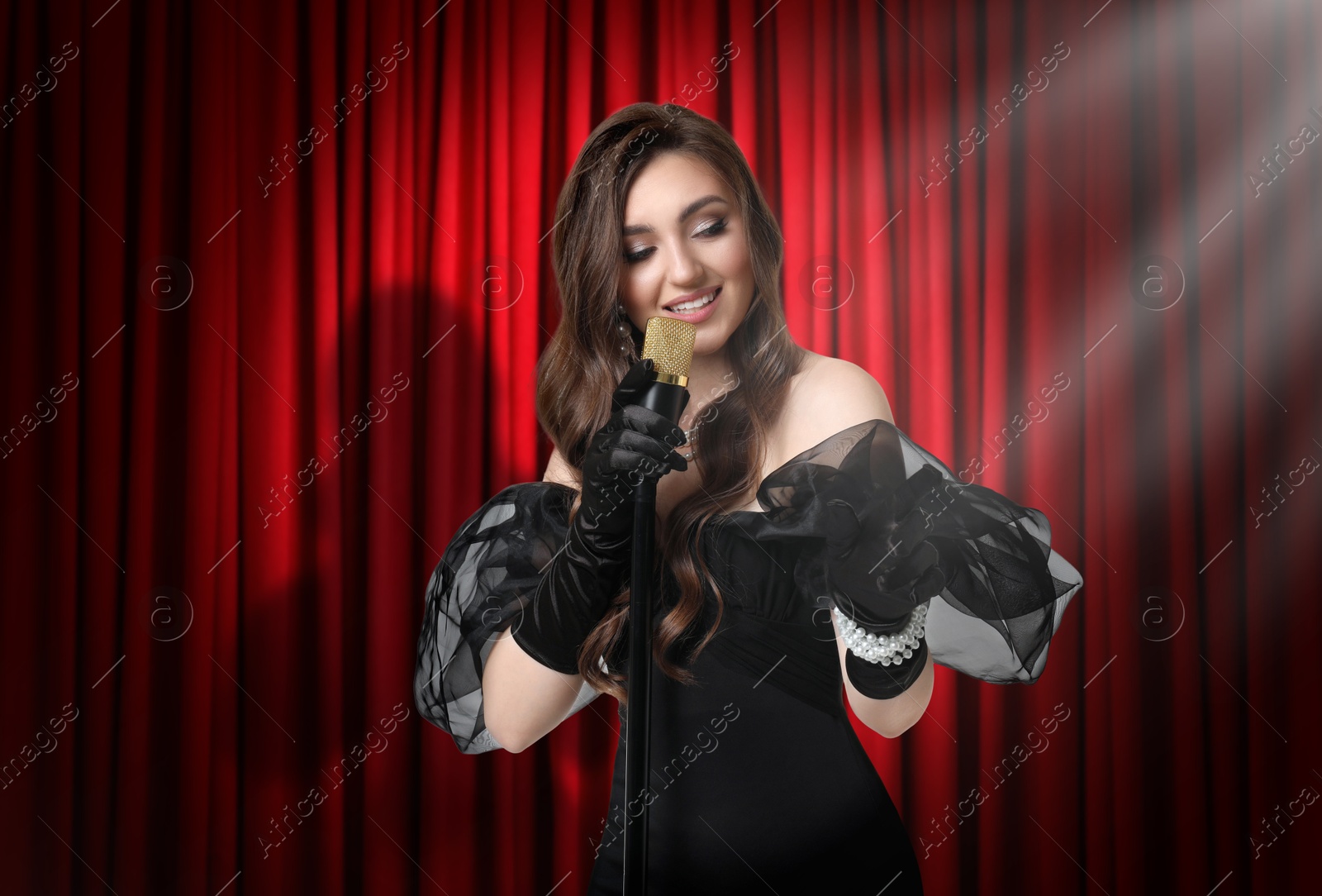 Image of Beautiful singer performing in spotlight on stage against red curtain