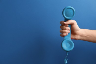 Woman holding telephone handset on blue background, closeup. Space for text