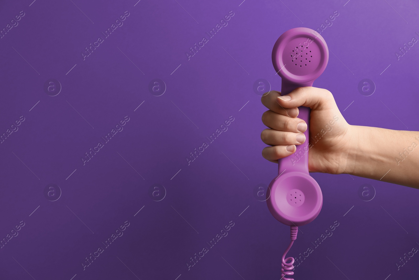 Image of Woman holding telephone handset on purple background, closeup. Space for text