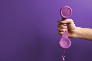 Woman holding telephone handset on purple background, closeup. Space for text