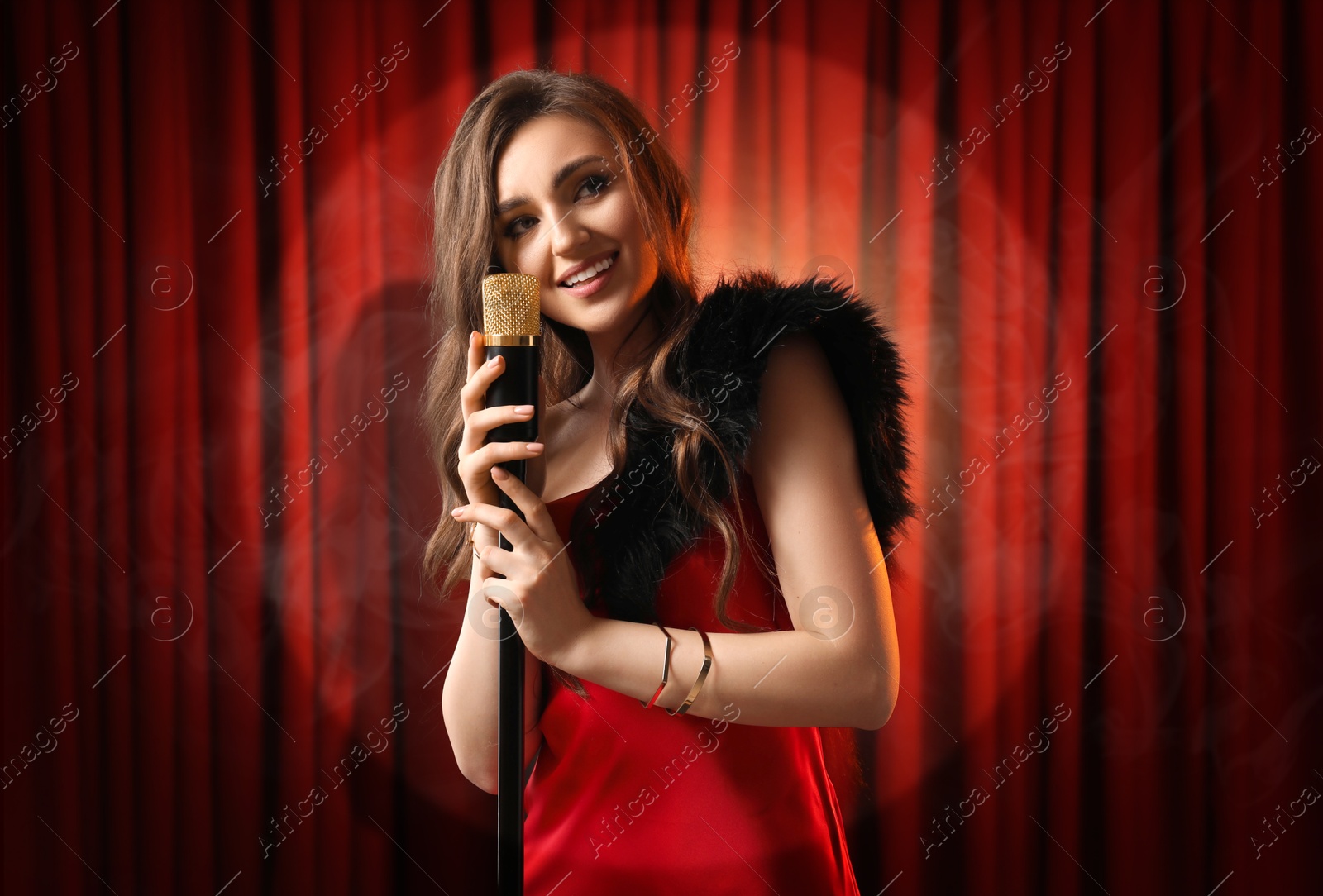 Image of Beautiful singer performing in spotlight on stage against red curtain