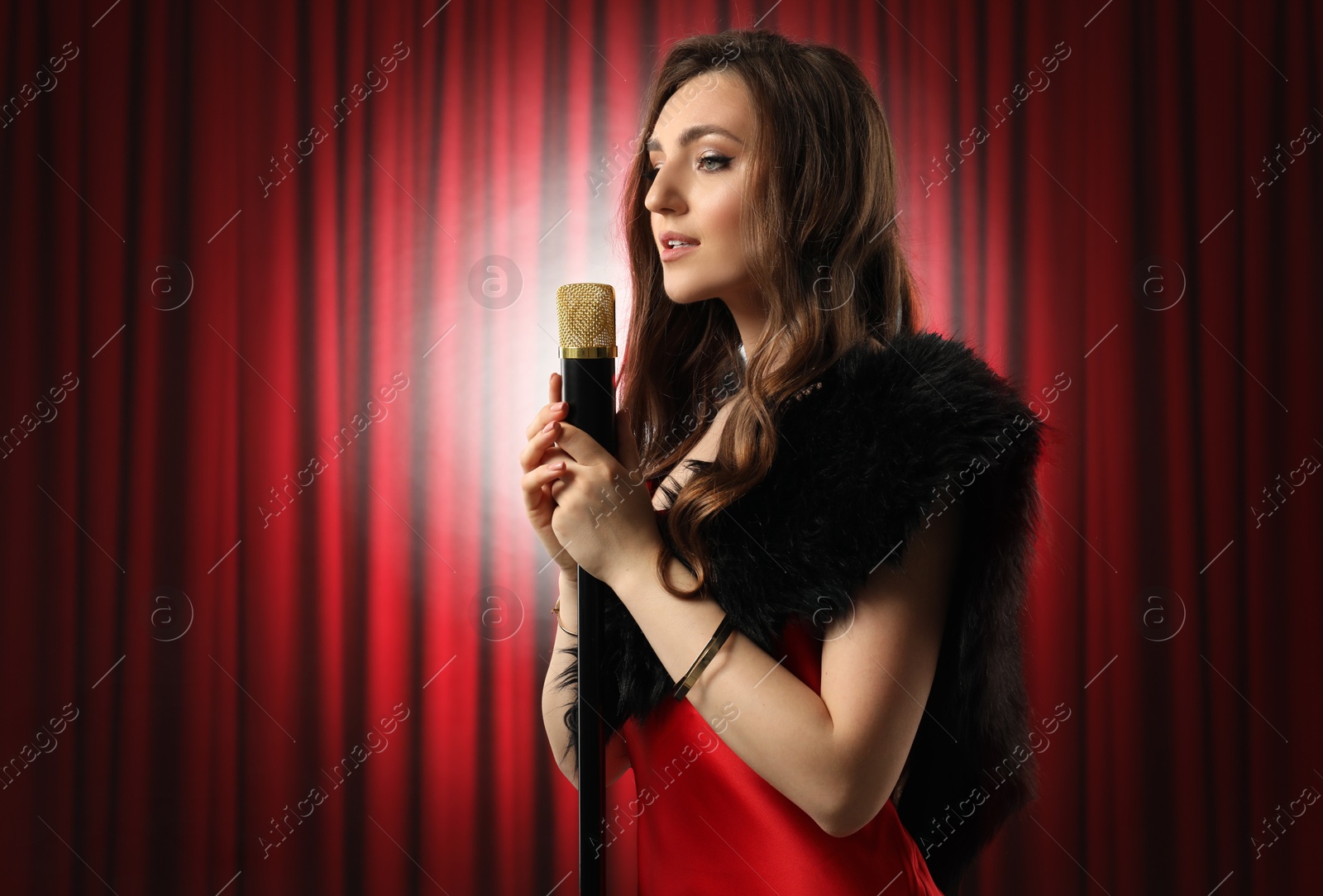 Image of Beautiful singer performing in spotlight on stage against red curtain