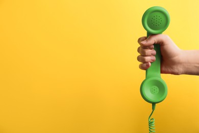 Image of Woman holding green telephone handset on yellow background, closeup. Space for text