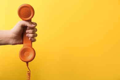 Woman holding orange telephone handset on yellow background, closeup. Space for text