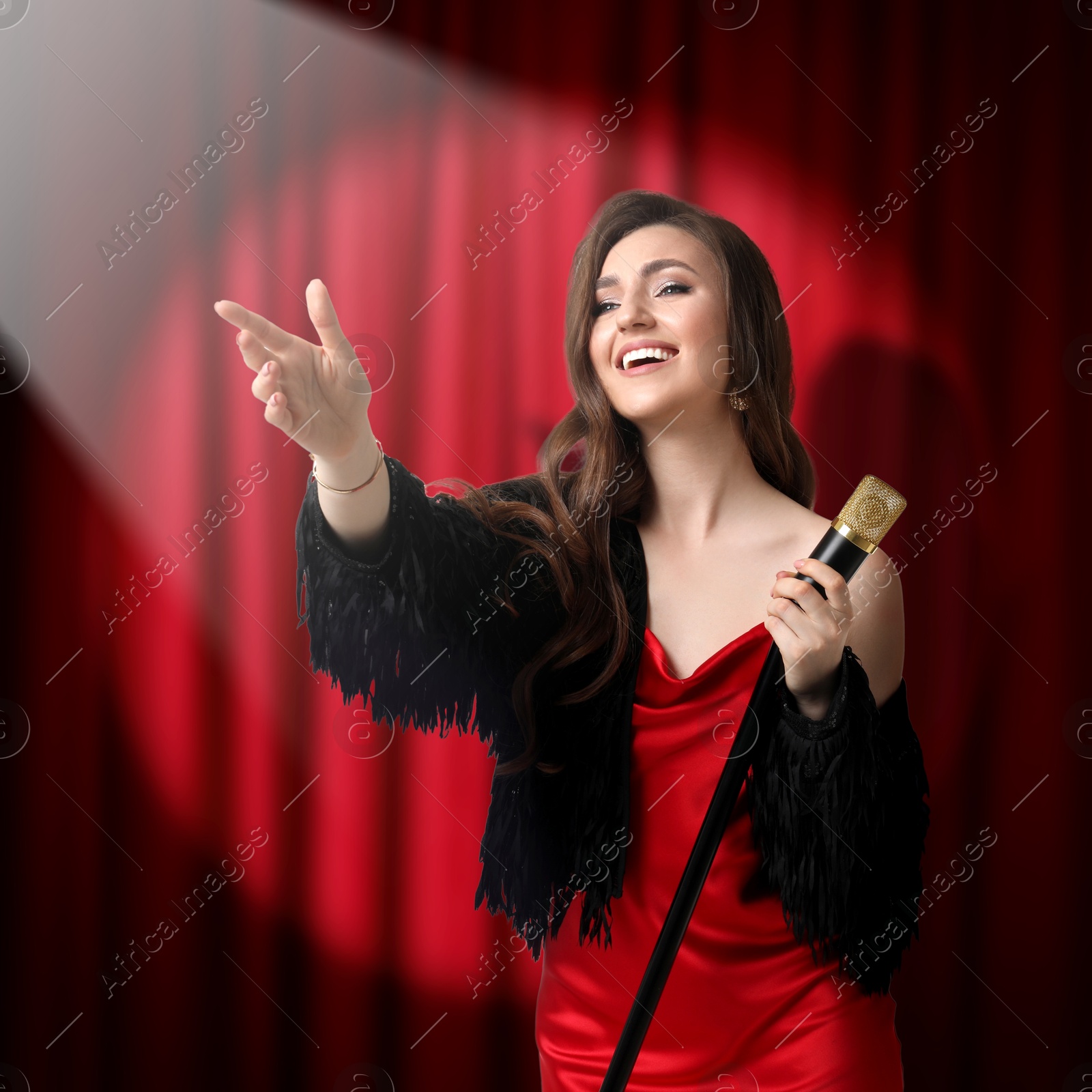 Image of Beautiful singer performing in spotlight on stage against red curtain
