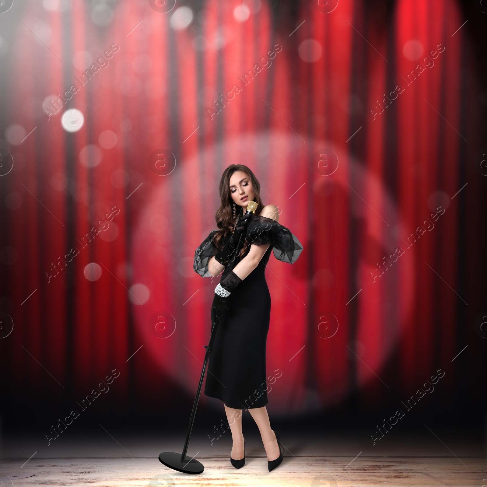 Image of Beautiful singer performing in spotlight on stage against red curtain