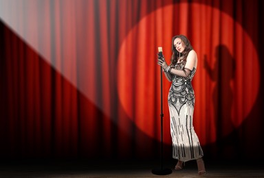 Beautiful singer performing in spotlight on stage against red curtain. Space for text