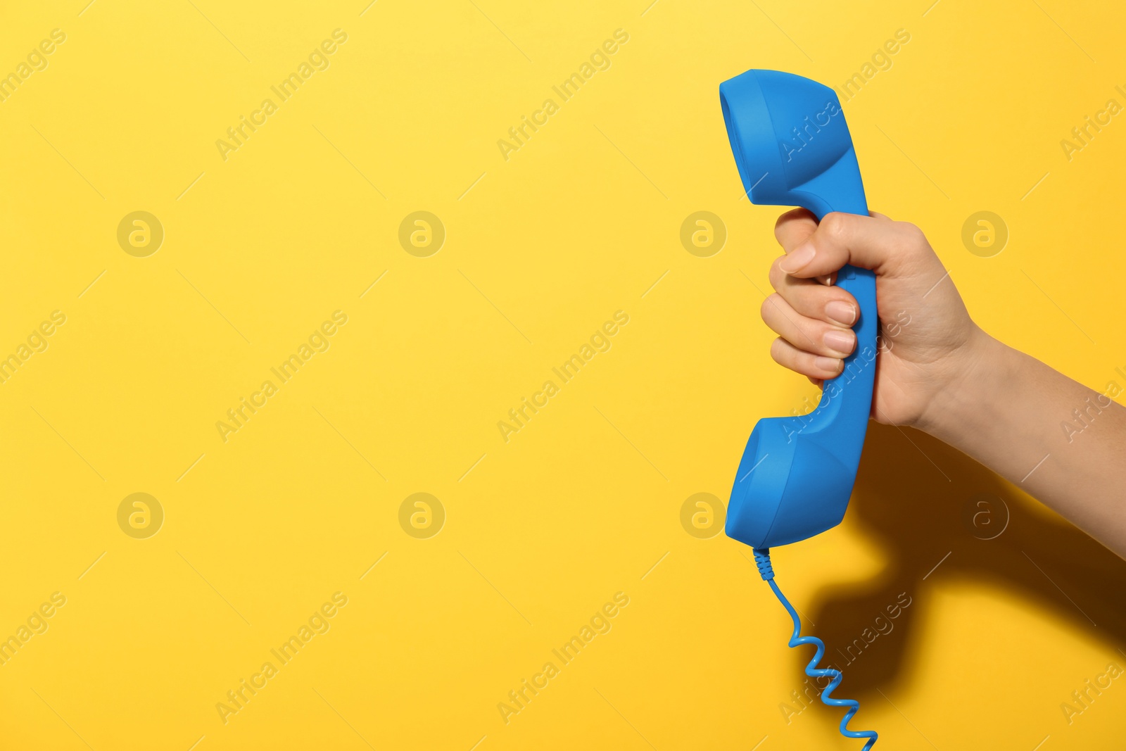 Image of Woman holding blue telephone handset on yellow background, closeup. Space for text