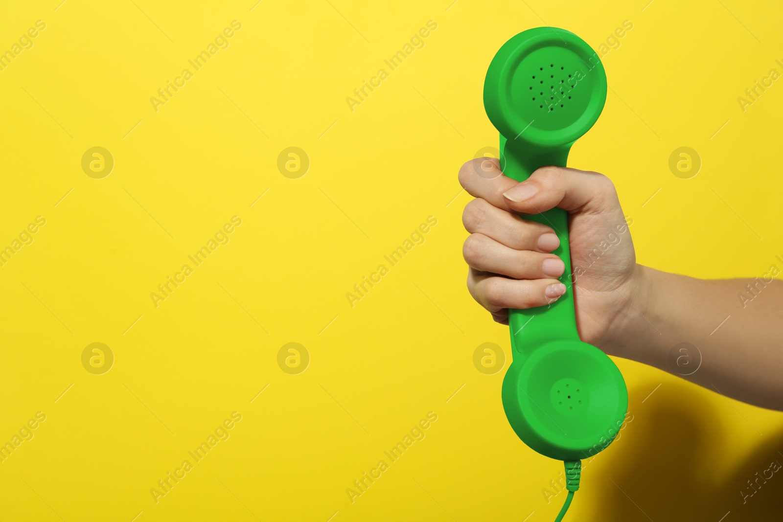 Image of Woman holding green telephone handset on yellow background, closeup. Space for text