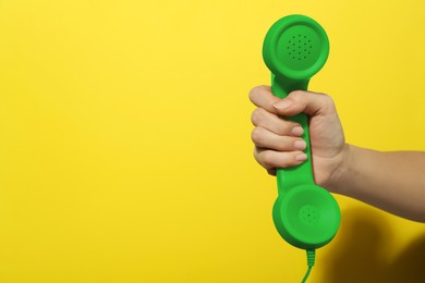 Woman holding green telephone handset on yellow background, closeup. Space for text