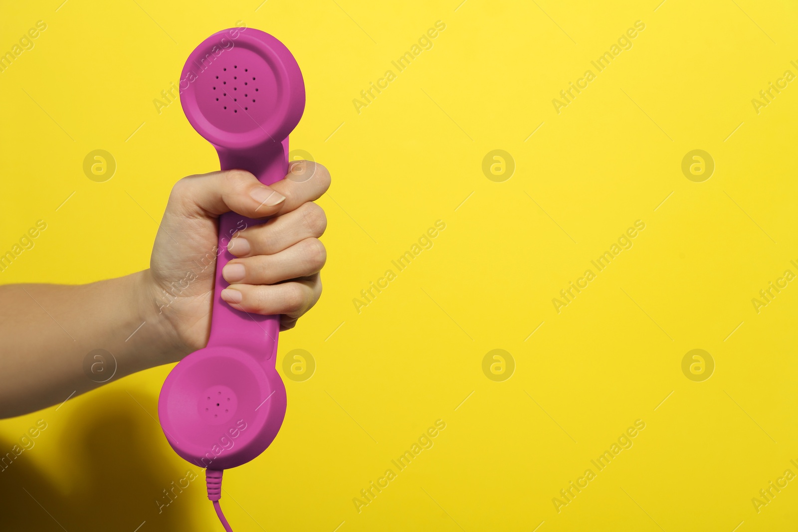 Image of Woman holding magenta telephone handset on yellow background, closeup. Space for text