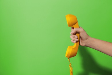 Woman holding yellow telephone handset on green background, closeup. Space for text
