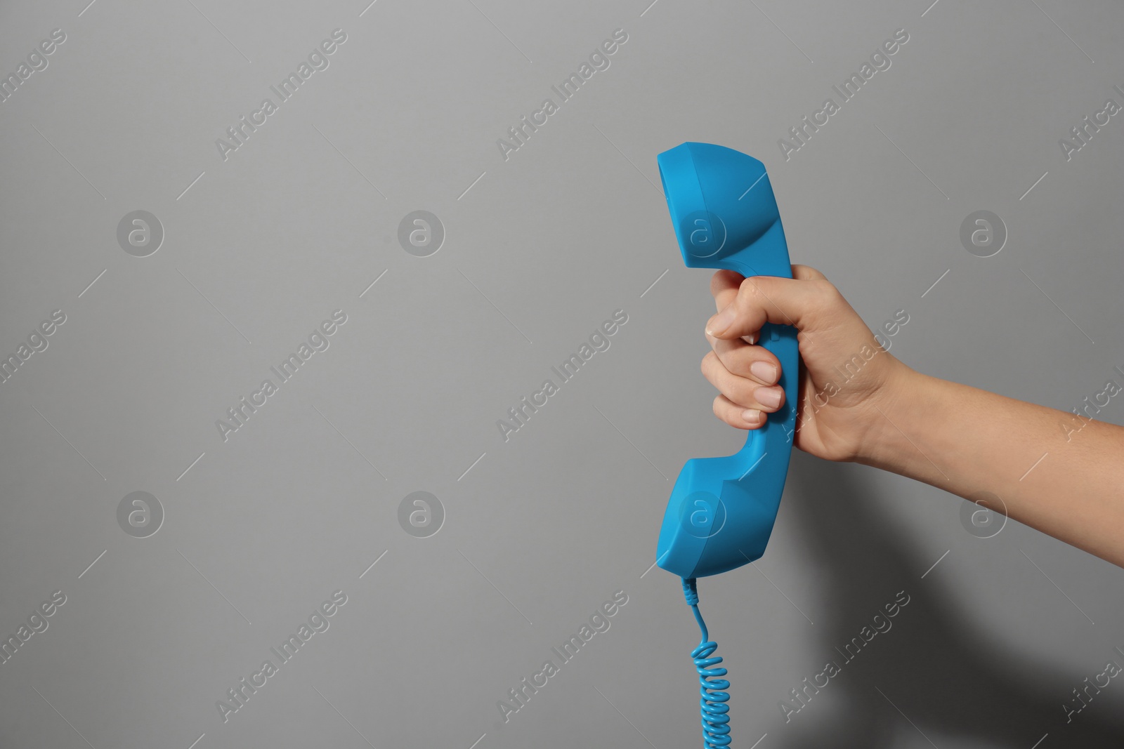 Image of Woman holding blue telephone handset on light grey background, closeup. Space for text