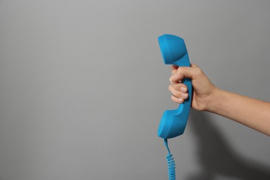 Woman holding blue telephone handset on light grey background, closeup. Space for text