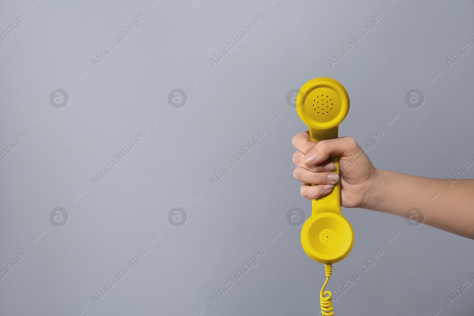 Image of Woman holding yellow telephone handset on light grey background, closeup. Space for text