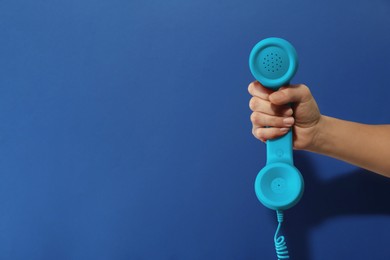 Woman holding telephone handset on blue background, closeup. Space for text